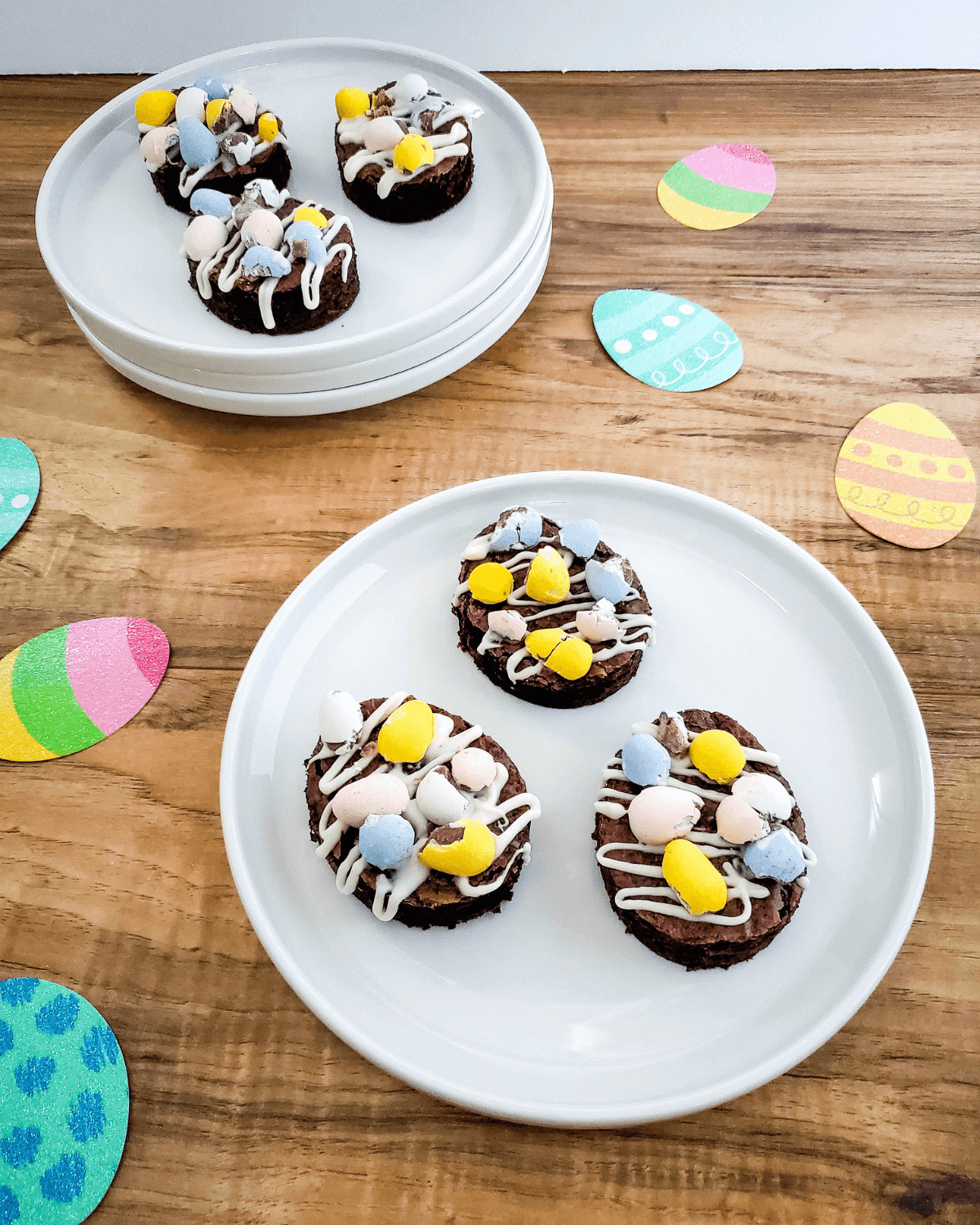 A dessert with candy eggs and drizzled icing on a wooden table with Easter-themed paper plates.