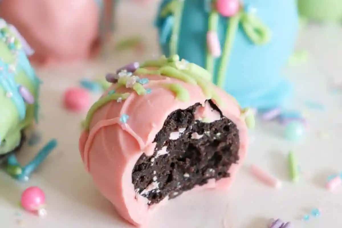 A pink chocolate-covered Oreo ball with a bite taken out reveals a dark, crumbly interior. Perfect as Easter treats for kids, its top is adorned with green icing and sprinkles, creating an enticing festive delight.