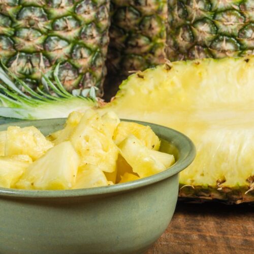 A bowl of cut up pineapple with whole pineapple in the background.