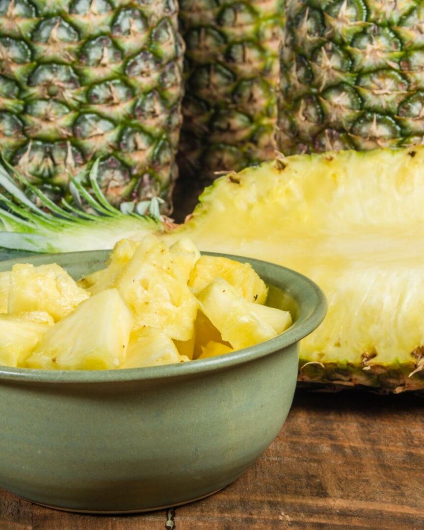A bowl of cut up pineapple with whole pineapple in the background.