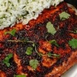 A fillet, expertly grilled and seasoned, garnished with cilantro, served alongside herb-infused white rice on a white plate.
