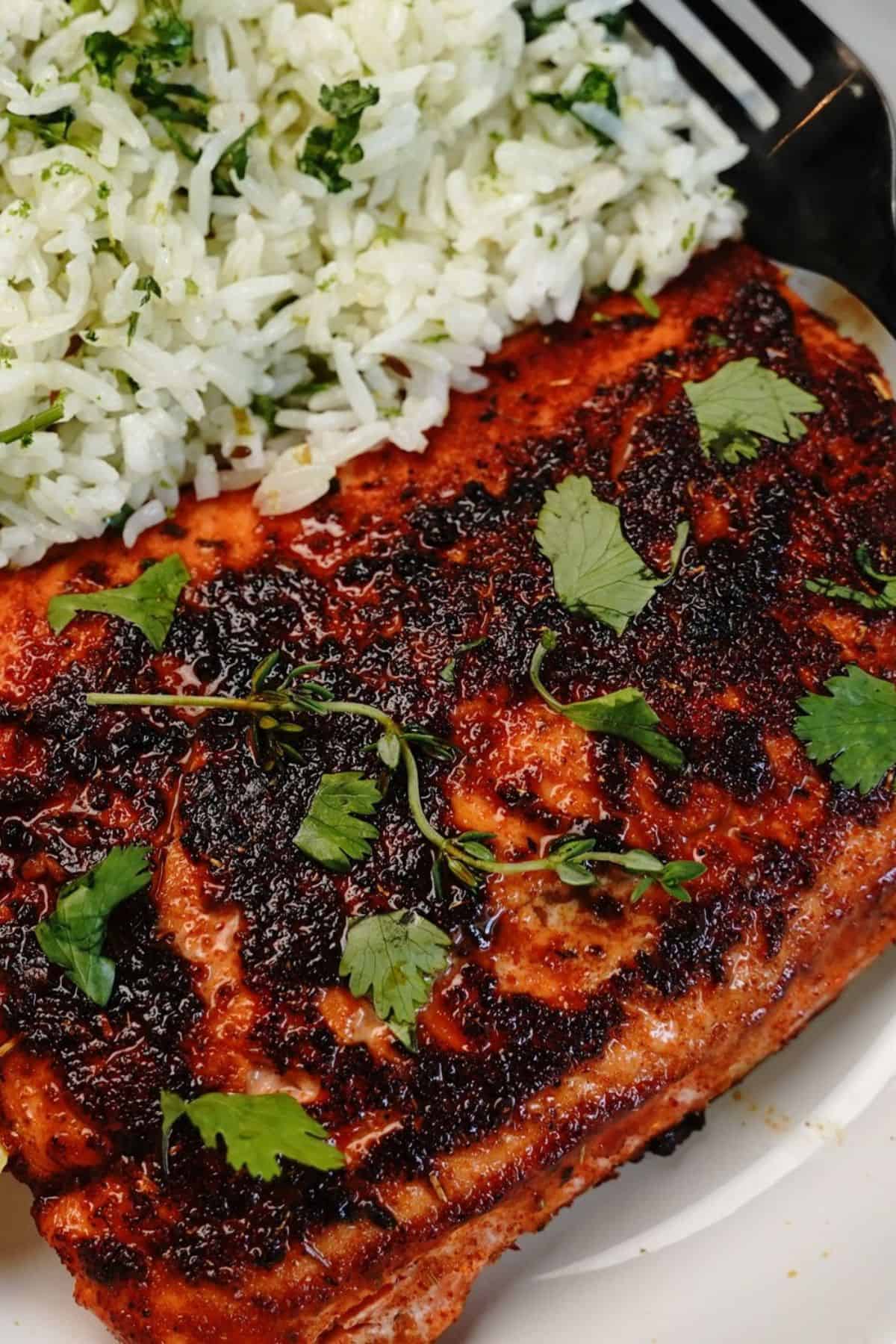 A fillet, expertly grilled and seasoned, garnished with cilantro, served alongside herb-infused white rice on a white plate.