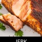 A close-up of a cooked jerk salmon fillet on a white plate, garnished with parsley, with one piece sliced off to showcase the flavorful seasoning.