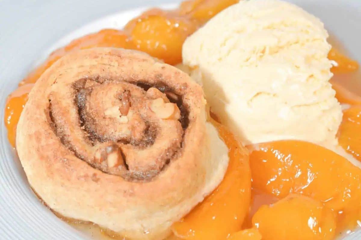 A peach cobbler with nuts, a scoop of vanilla ice cream, and sliced peaches on a white plate makes the perfect Easter treat for kids.