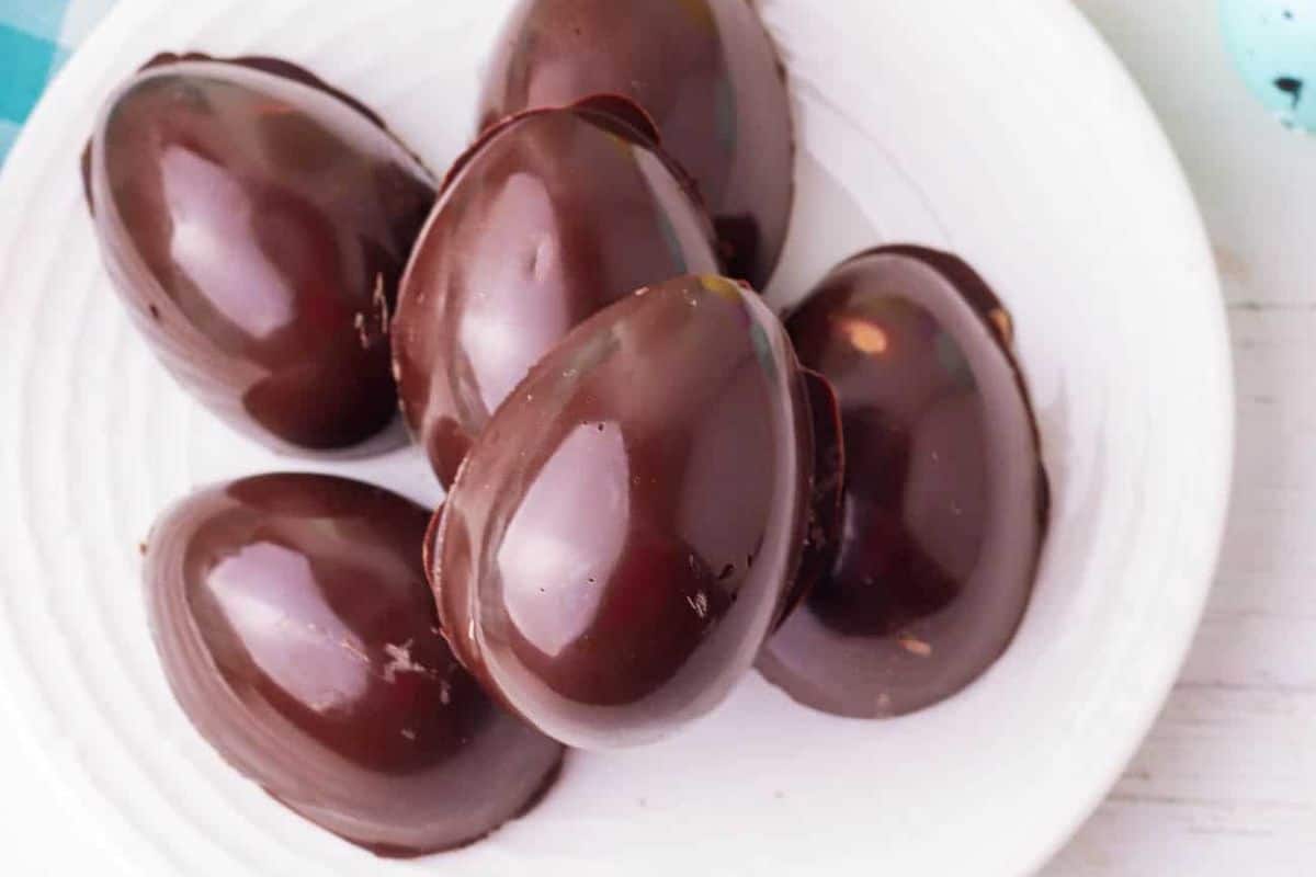 Five glossy, peanut butter Easter eggs arranged on a white plate, perfect as delightful Easter treats for kids.