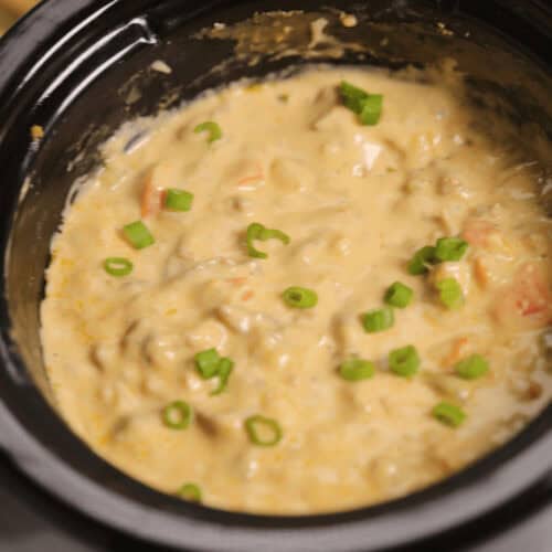 A crockpot filled with creamy soup, reminiscent of a Philly Cheesesteak Dip, topped with chopped green onions.