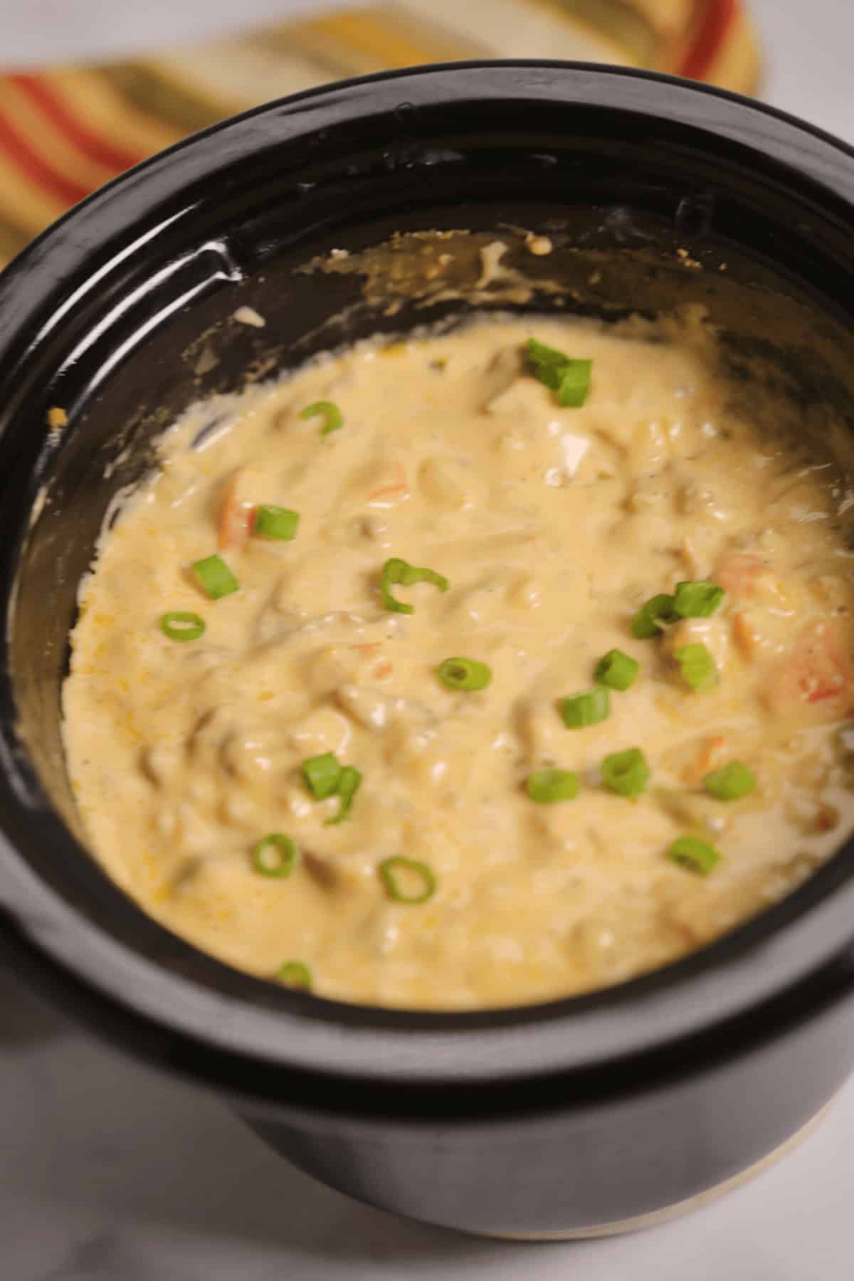 A crockpot filled with creamy soup, reminiscent of a Philly Cheesesteak Dip, topped with chopped green onions.