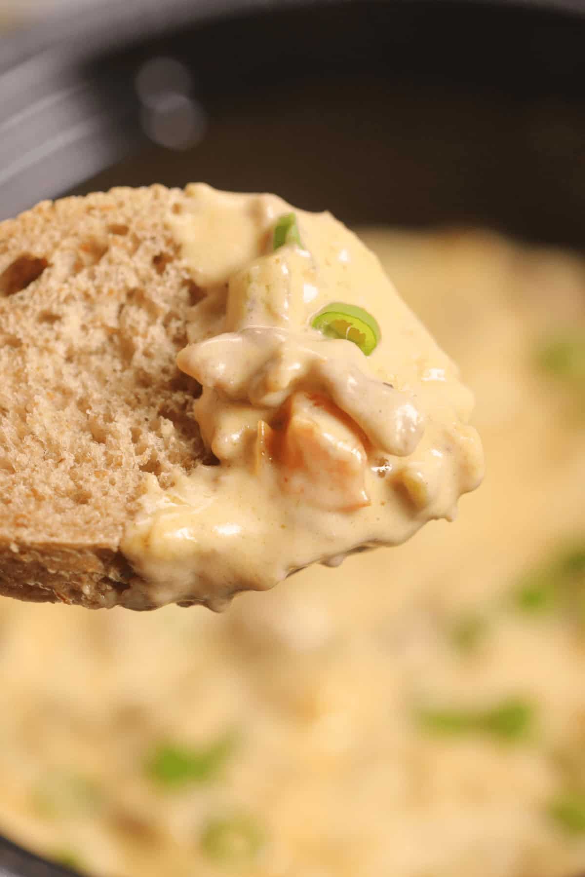 A slice of bread topped with creamy Philly Cheesesteak Dip, garnished with chopped green onions.