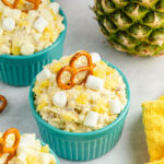 A turquoise bowl of pineapple fluff with a pretzel on top.
