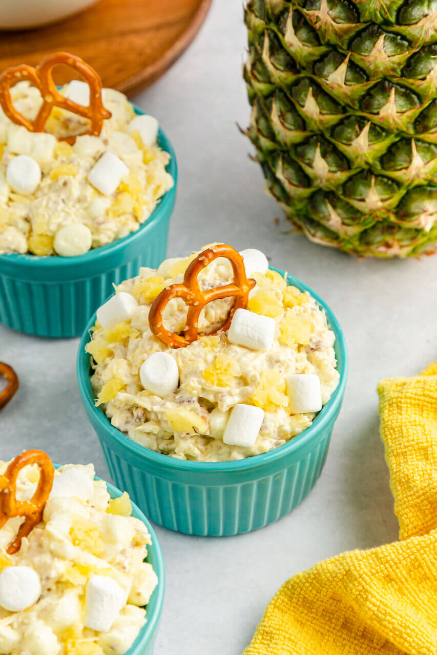 A turquoise bowl of pineapple fluff with a pretzel on top.