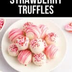 A plate of delicious strawberry truffles coated in white chocolate, decorated with pink drizzle and red and pink sprinkles, surrounded by small bowls of extra sprinkles.