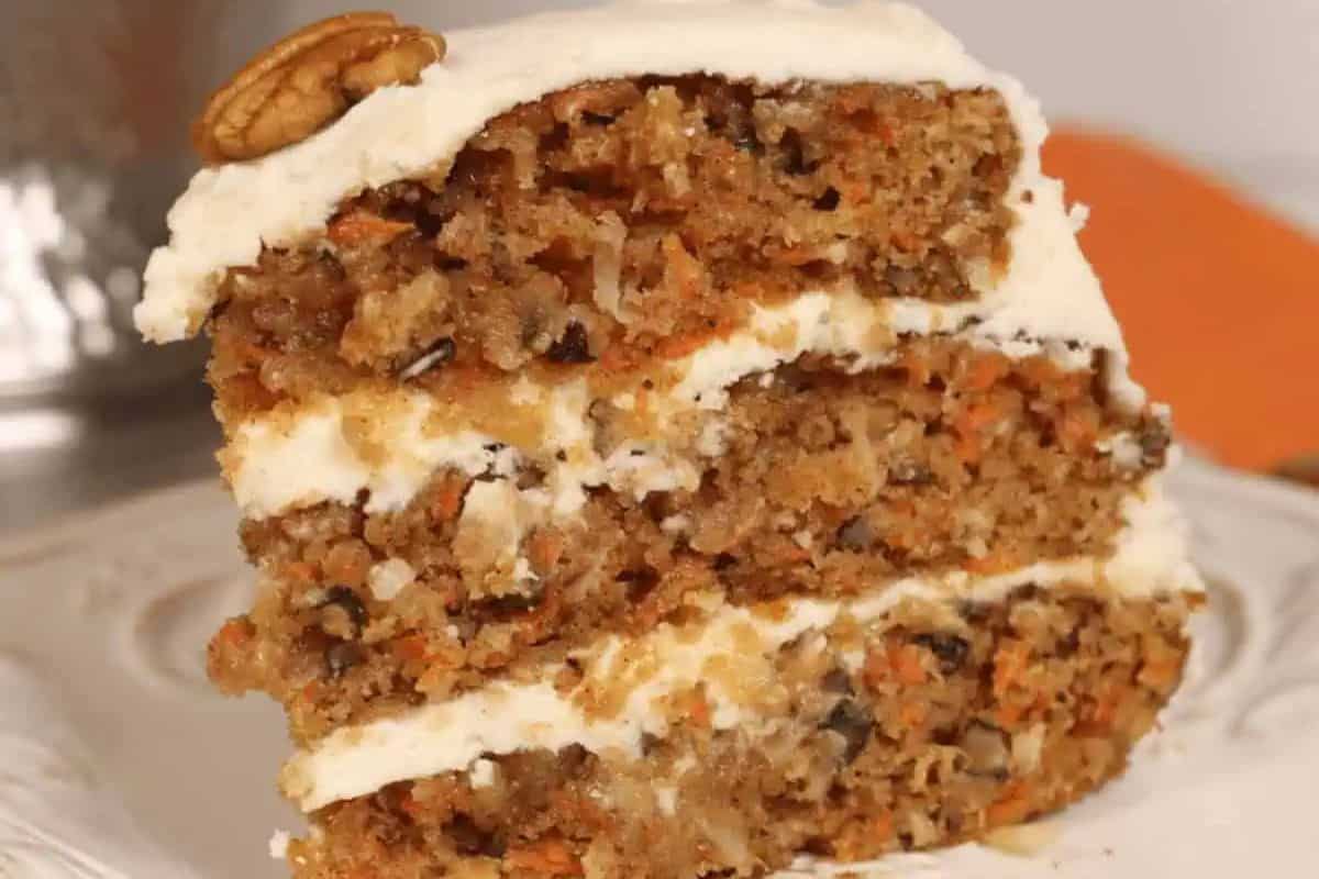 Slice of layered carrot cake with cream cheese frosting and a walnut on top, served on a white plate—an ideal Easter treat for kids.