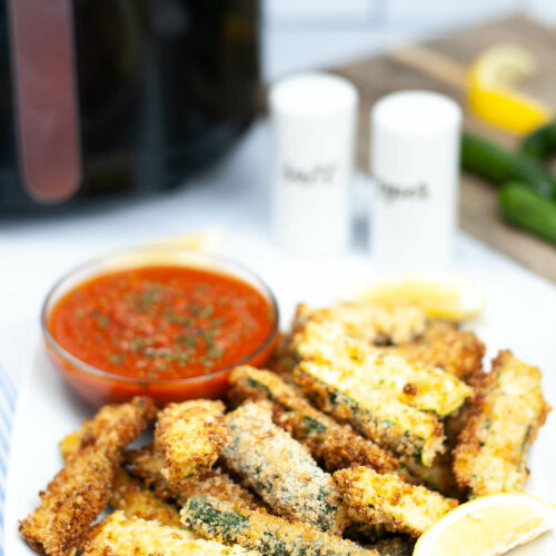 A white plate of air fryer zucchini fries with dipping sauce.