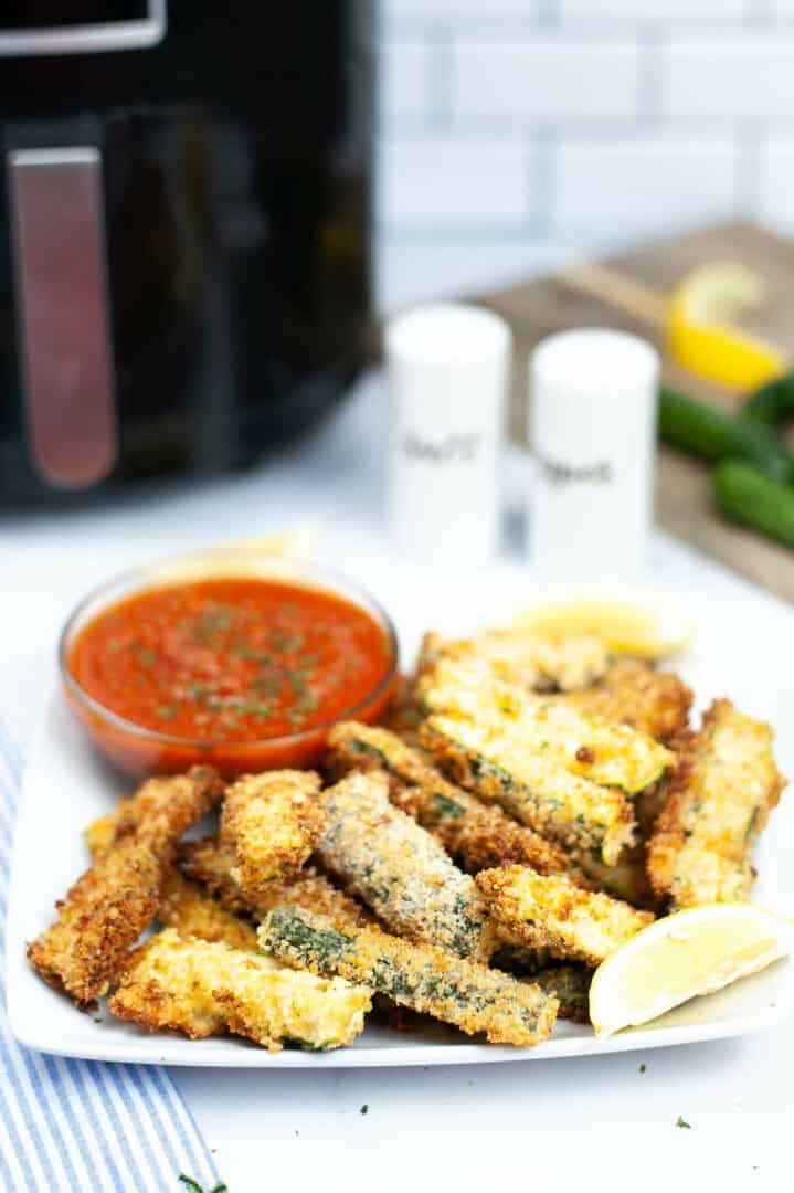 A white plate of air fryer zucchini fries with dipping sauce.
