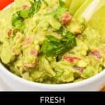Bowl of guacamole garnished with cilantro and lime wedges, with tomatoes and tortilla chips in the background. Text reads: "Fresh 4-Ingredient Guacamole Recipe.