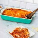 A casserole dish with the spaghetti and a white plate with a serving on it.