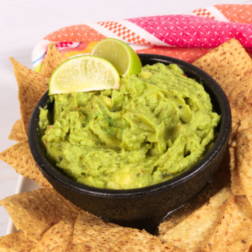 A bowl of easy Chunky Guacamole surrounded by tortilla chips.
