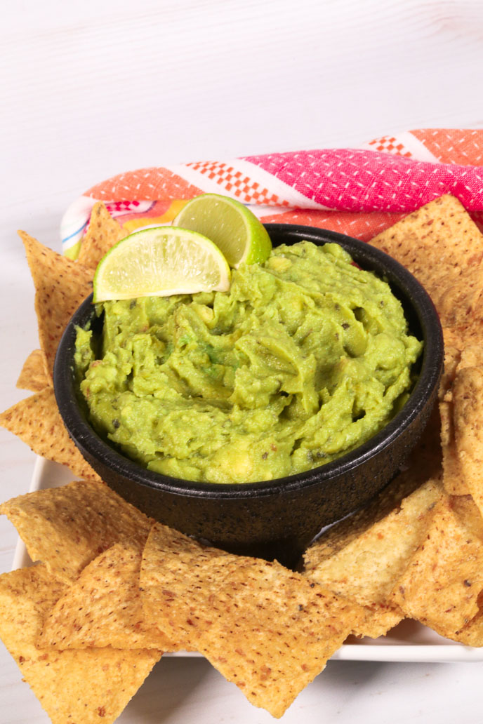 A bowl of easy Chunky Guacamole surrounded by tortilla chips.