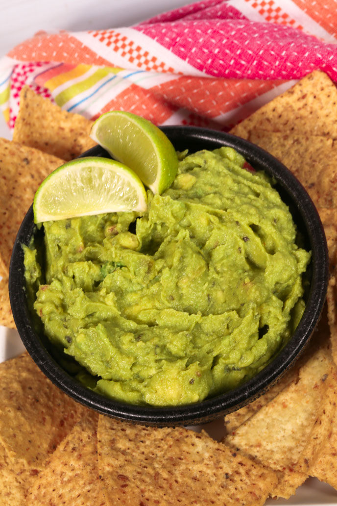 A bowl of the guacamole with slices of lime.