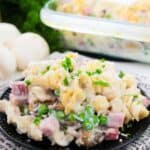 A black plate with ham and noodle casserole.