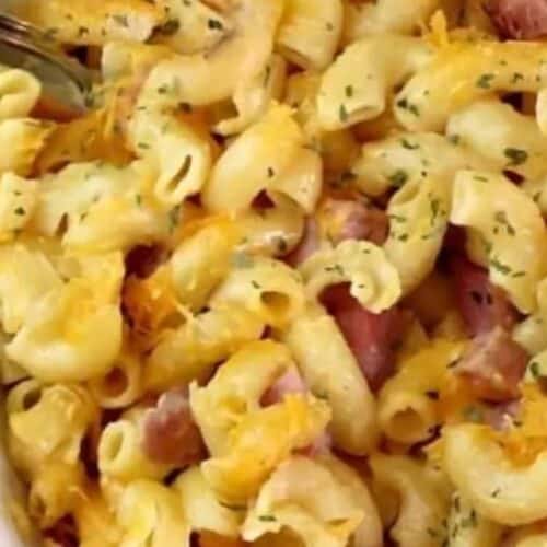 Baked macaroni and cheese with chunks of leftover ham, garnished with herbs in a white dish.