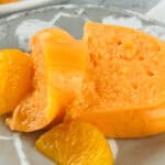Close-up of a sliced orange mousse with orange segments on a marble-patterned plate, reminiscent of an elegant Orange Jello Salad.