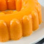A round fruity dessert sits in a glossy, smooth gelatin mold on a white plate atop the marble countertop.