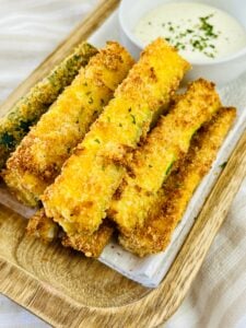A stack of oven baked zucchini sticks on a tray with dipping sauce.