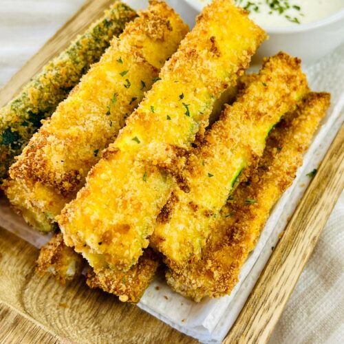 A stack of oven baked zucchini sticks on a tray with dipping sauce.