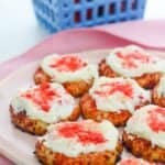 A plate of the treats topped with white frosting and red sprinkles, with a blue basket of strawberries in the background.