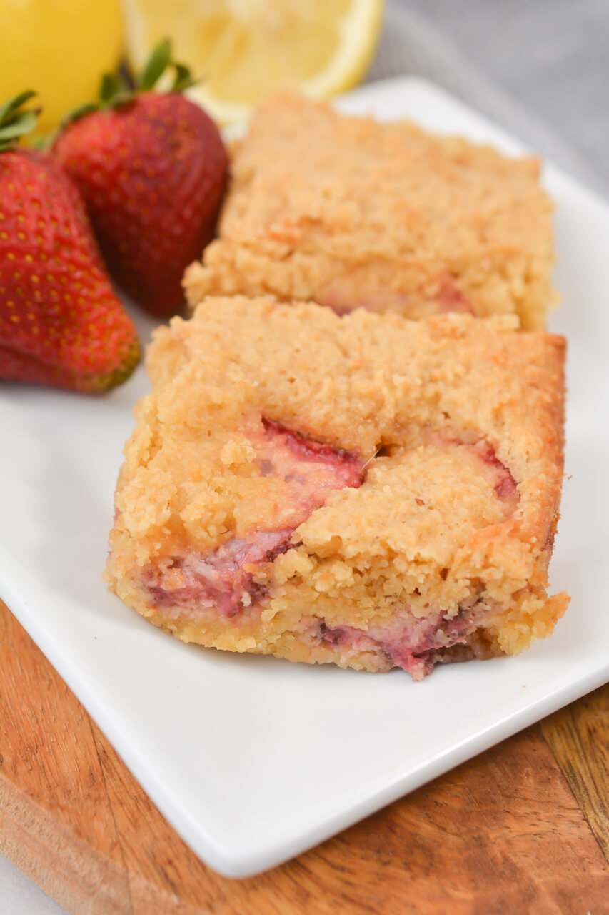 A strawberry lemon blondie on a white plate with strawberries on the side.