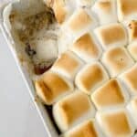 A baking dish filled with golden-brown toasted marshmallows with one corner deliciously scooped out.