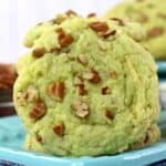 A round, light green Pistachio Pudding Cookie topped with chopped pecans sits on a blue plate.