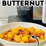 Bowl of crispy, seasoned Air Fryer Butternut Squash cubes on a table, with an air fryer appliance in the background.