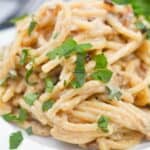 A plate of creamy caramelized onion pasta topped with chopped fresh herbs on a white plate.