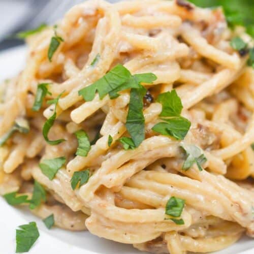 A plate of creamy caramelized onion pasta topped with chopped fresh herbs on a white plate.