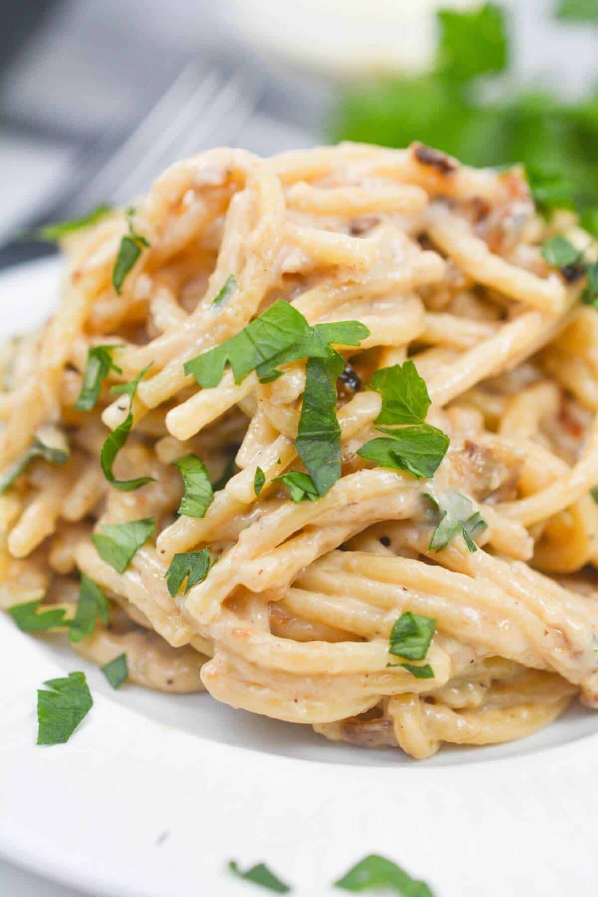A plate of creamy caramelized onion pasta topped with chopped fresh herbs on a white plate.