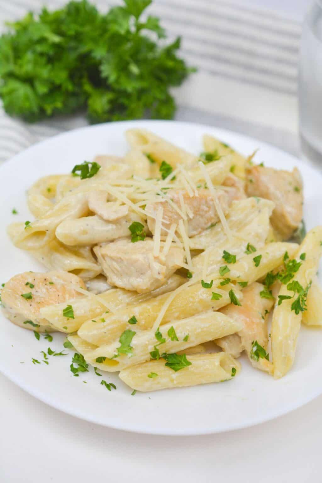Plate of penne pasta with creamy white sauce, pieces of Chicken Gorgonzola, grated cheese, and chopped parsley, served on a white dish.