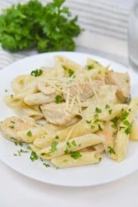 Plate of penne pasta with creamy white sauce, pieces of Chicken Gorgonzola, grated cheese, and chopped parsley, served on a white dish.