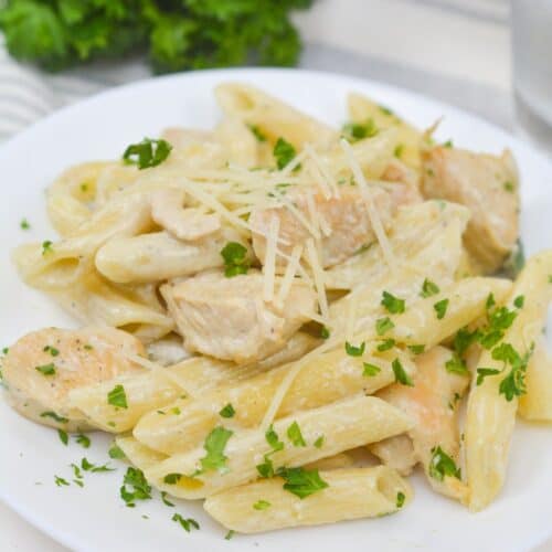 Plate of penne pasta with creamy white sauce, pieces of Chicken Gorgonzola, grated cheese, and chopped parsley, served on a white dish.
