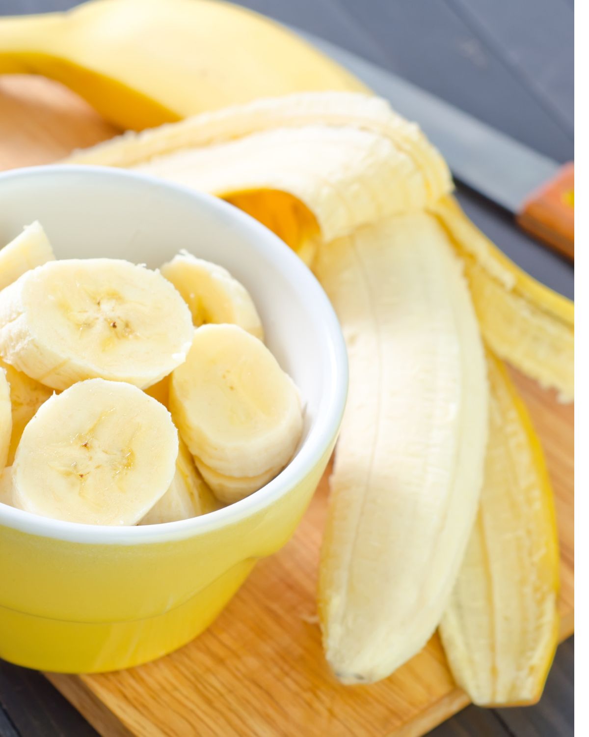 Banana slices in a yellow bowl with a whole banana on the side. 