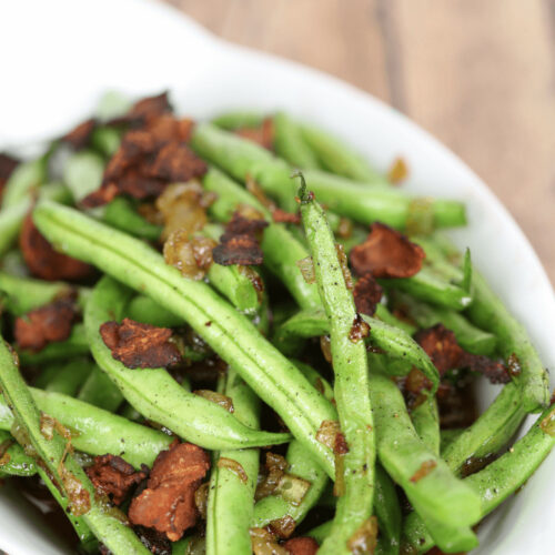 A white bowl of green beans, bacon and onions.
