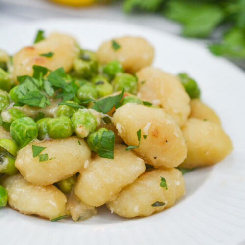 A white plate of gnocchi with peas.