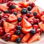 A plate filled with sliced strawberries, whole blueberries, cherries, and raspberries on a pink napkin makes a colorful Strawberry Blueberry Salad perfect for any occasion.