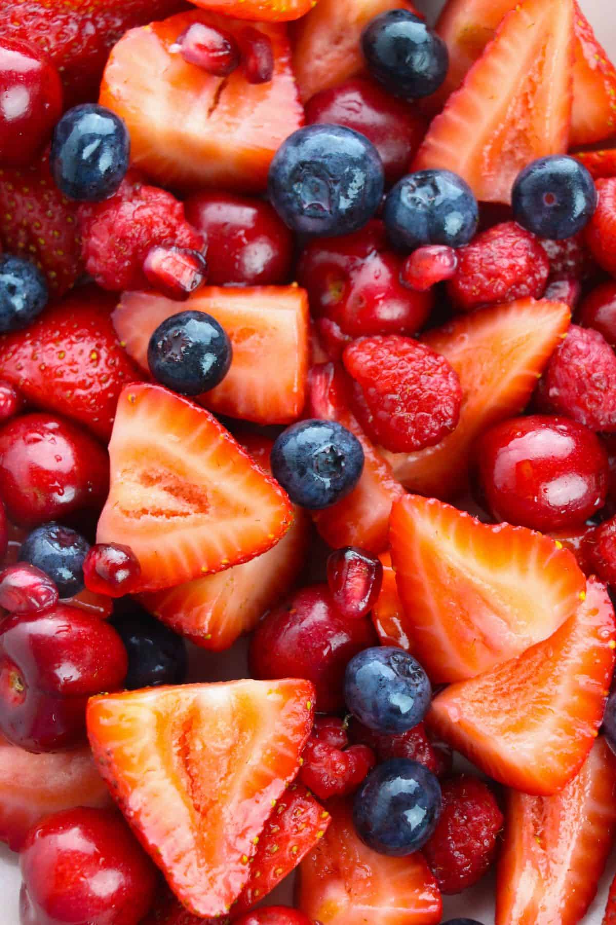 Close-up of a colorful Strawberry Blueberry Salad with fresh sliced strawberries, whole blueberries, raspberries, cherries, and pomegranate seeds.