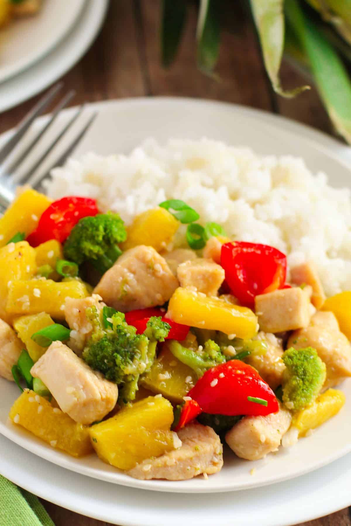 A plate of white rice served with Pineapple Chicken Stir Fry, featuring tender chicken, broccoli, red bell peppers, pineapple chunks, and green onions.