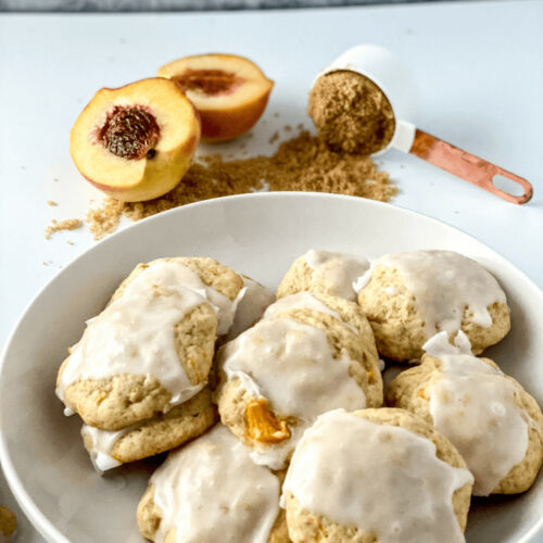 A white tray of peach cookies with a slice of peach on the side.