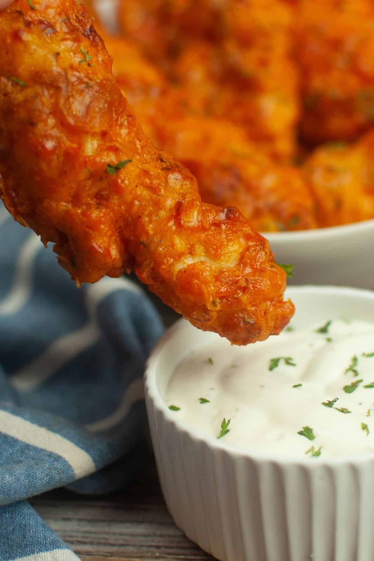 A piece  being dipped into a bowl of ranch dressing, with more  in the background..