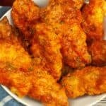 A bowl of crispy Air Fryer Buffalo Chicken wings is placed on a wooden surface with a blue napkin and a cup of dipping sauce nearby.