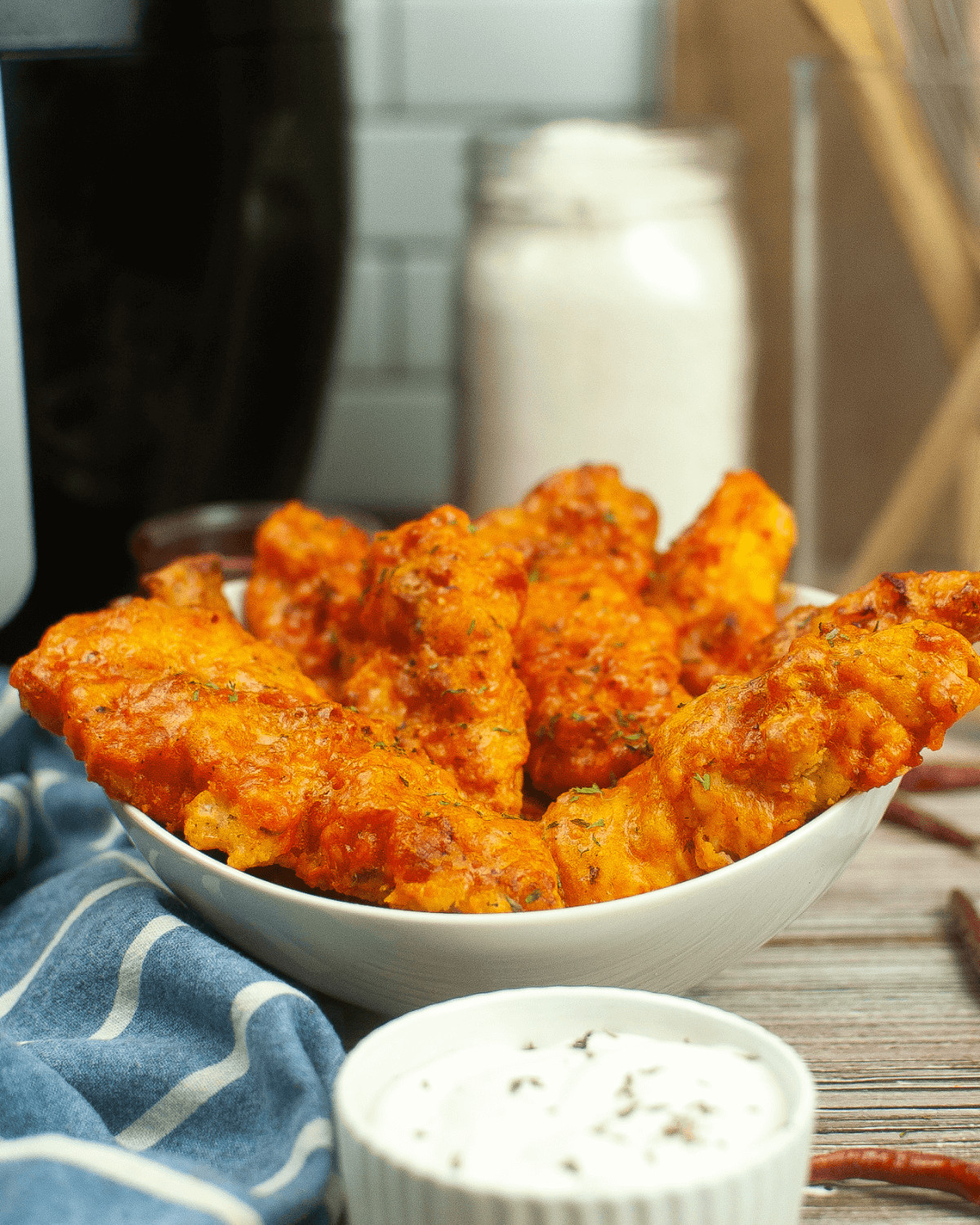 A heaping bowl of the air fryer buffalo chicken tenders with a side of dipping sauce.